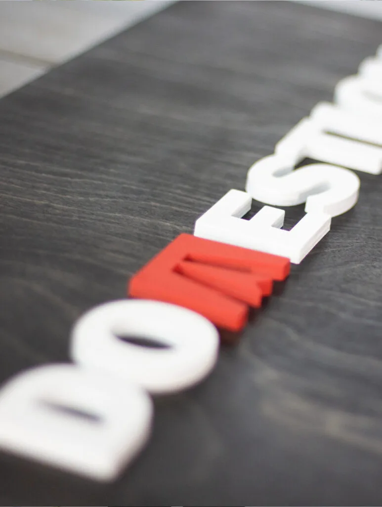 close-up of a black ebony stain sign with custom business logo made out of laser cut lettering. Red and white logo on a birch wood base.