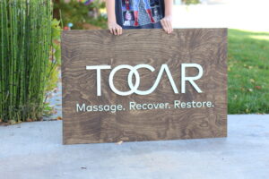 Custom logo wooden sign for a massage company - green and white logo on an aged walnut base