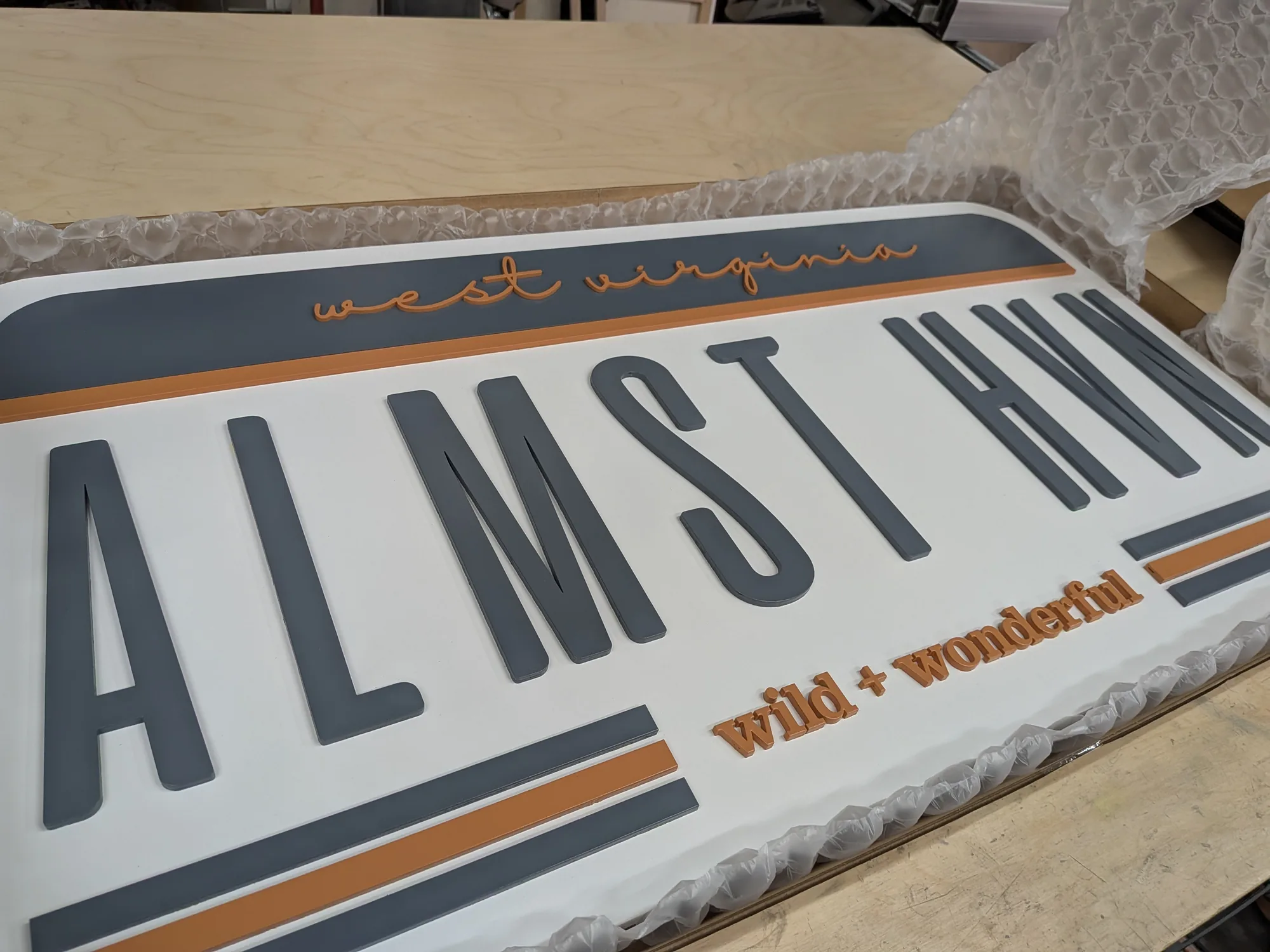 Giant custom license plate sign in painted white with gray and orange lettering