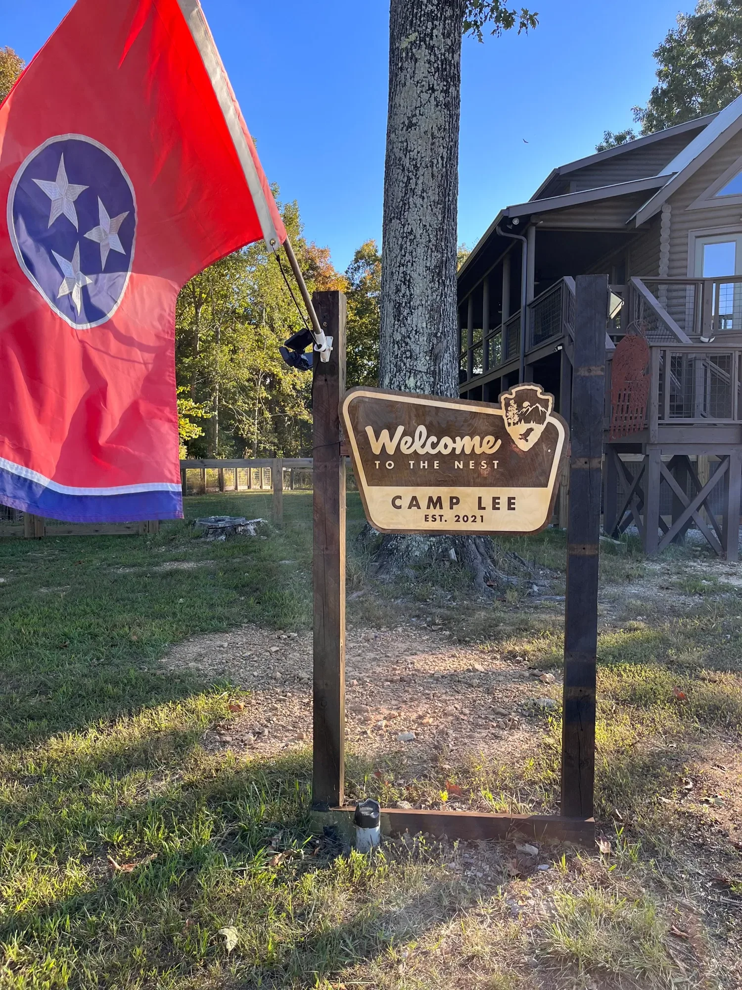 Park style welcome sign hanging from a wooden post frame outside a house